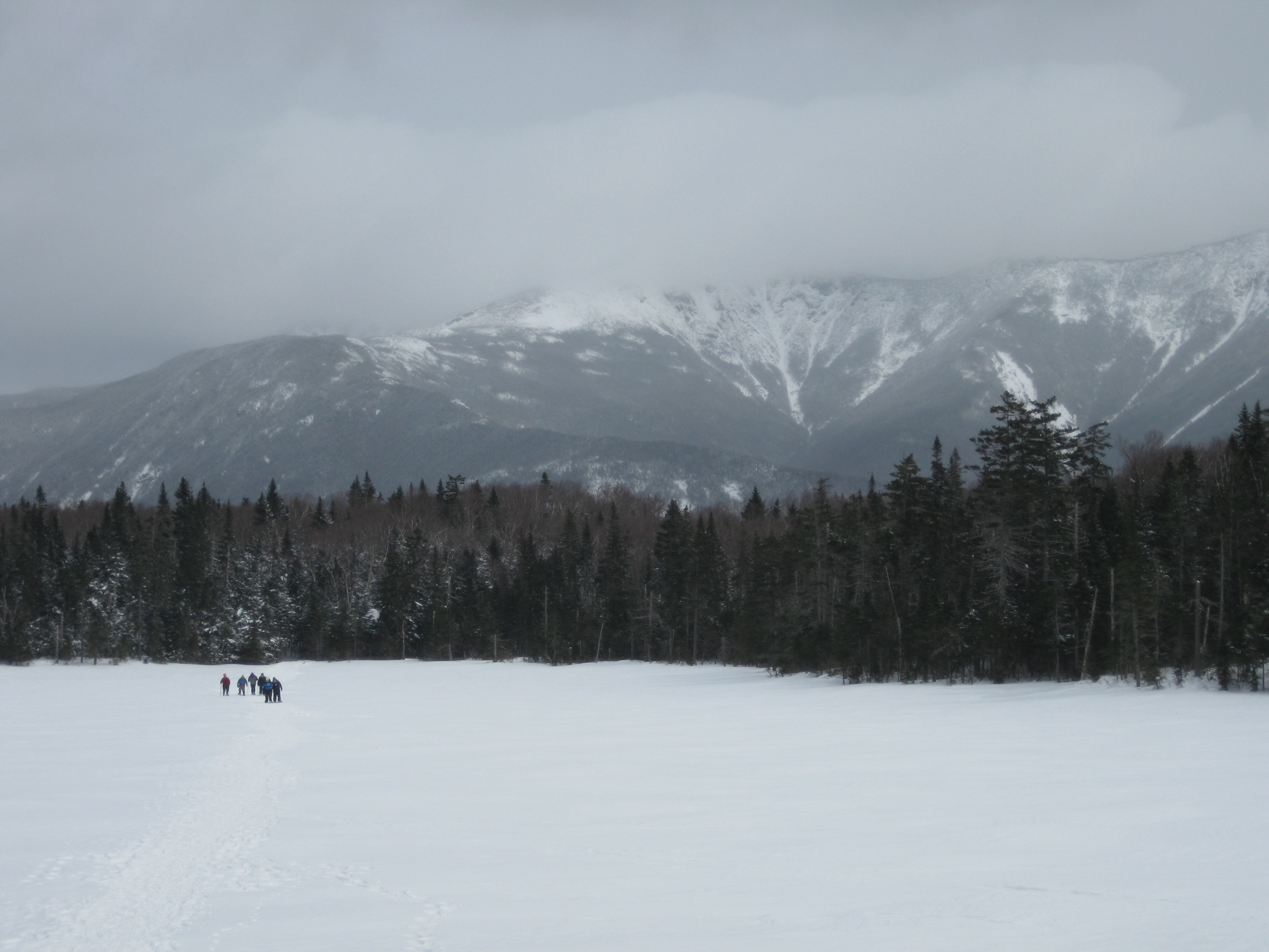 Winter hikers cross a very frozen Lonesome Lake to a backdrop of the majestic Franconia Ridge