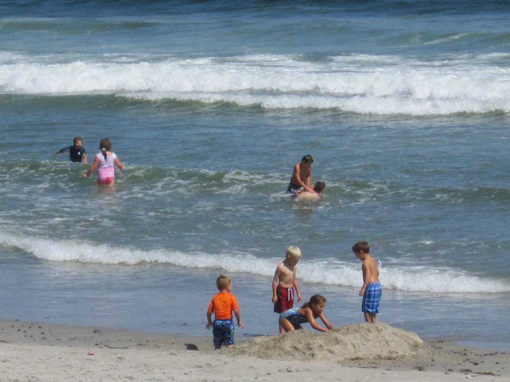 Random children attempt to drown each other in the Atlantic while others labor away on their sand castle. 